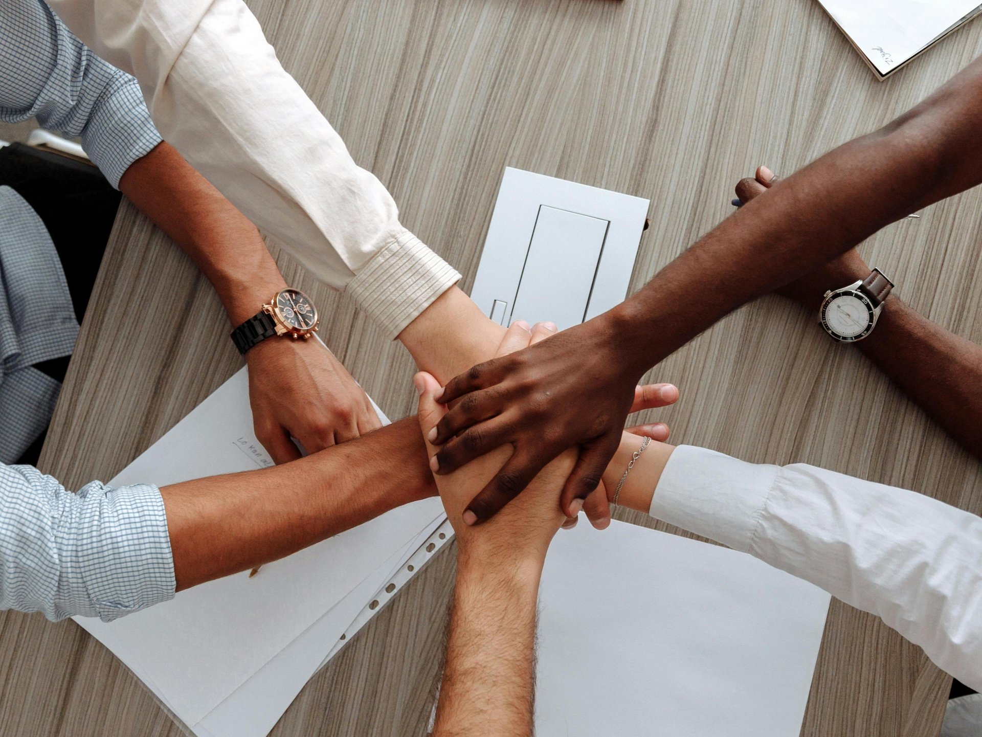 hands with different skin colour stack in unison above a table with documents