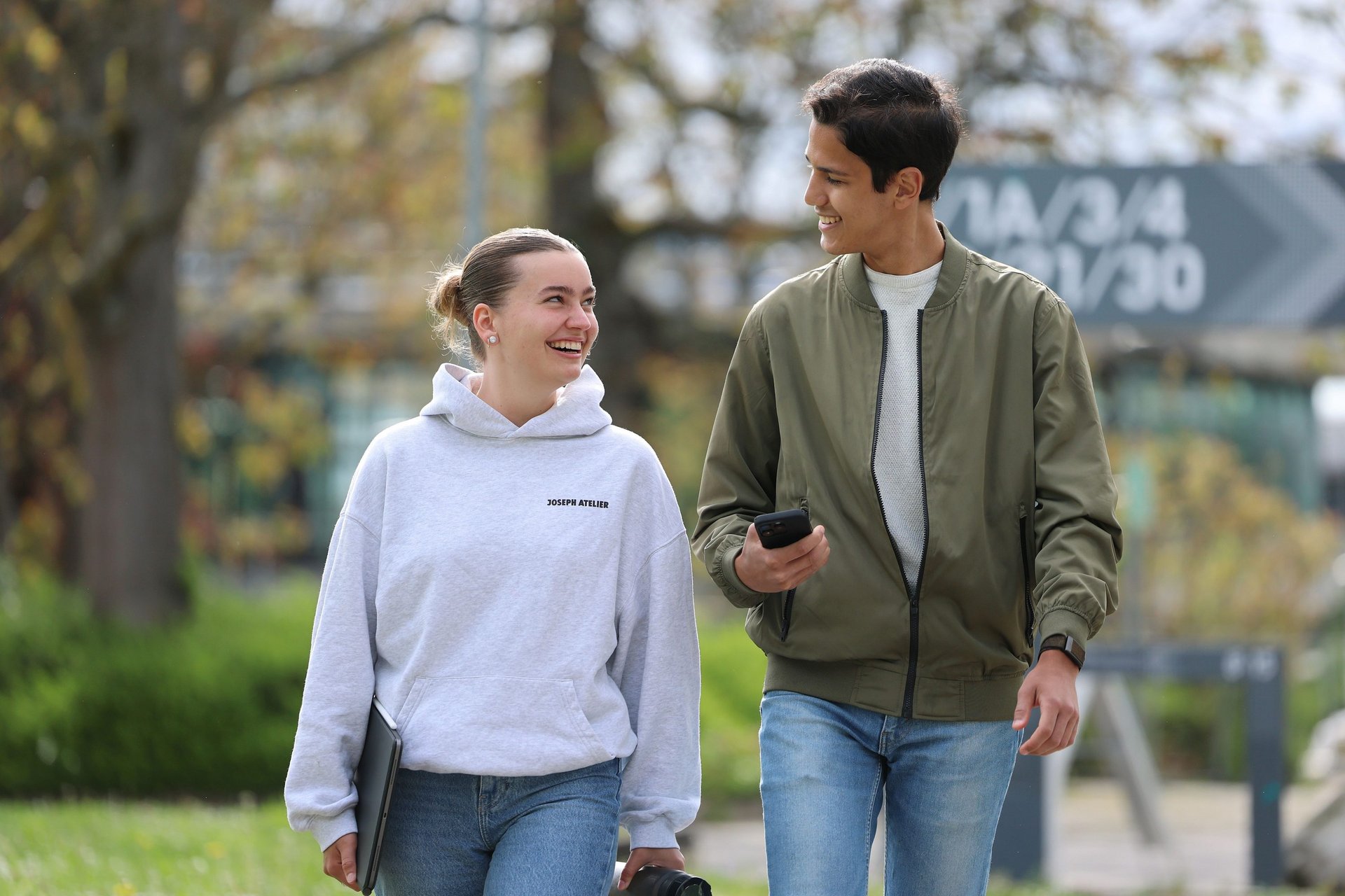 Zwei Studierende laufen über den Campus und lächeln sich an