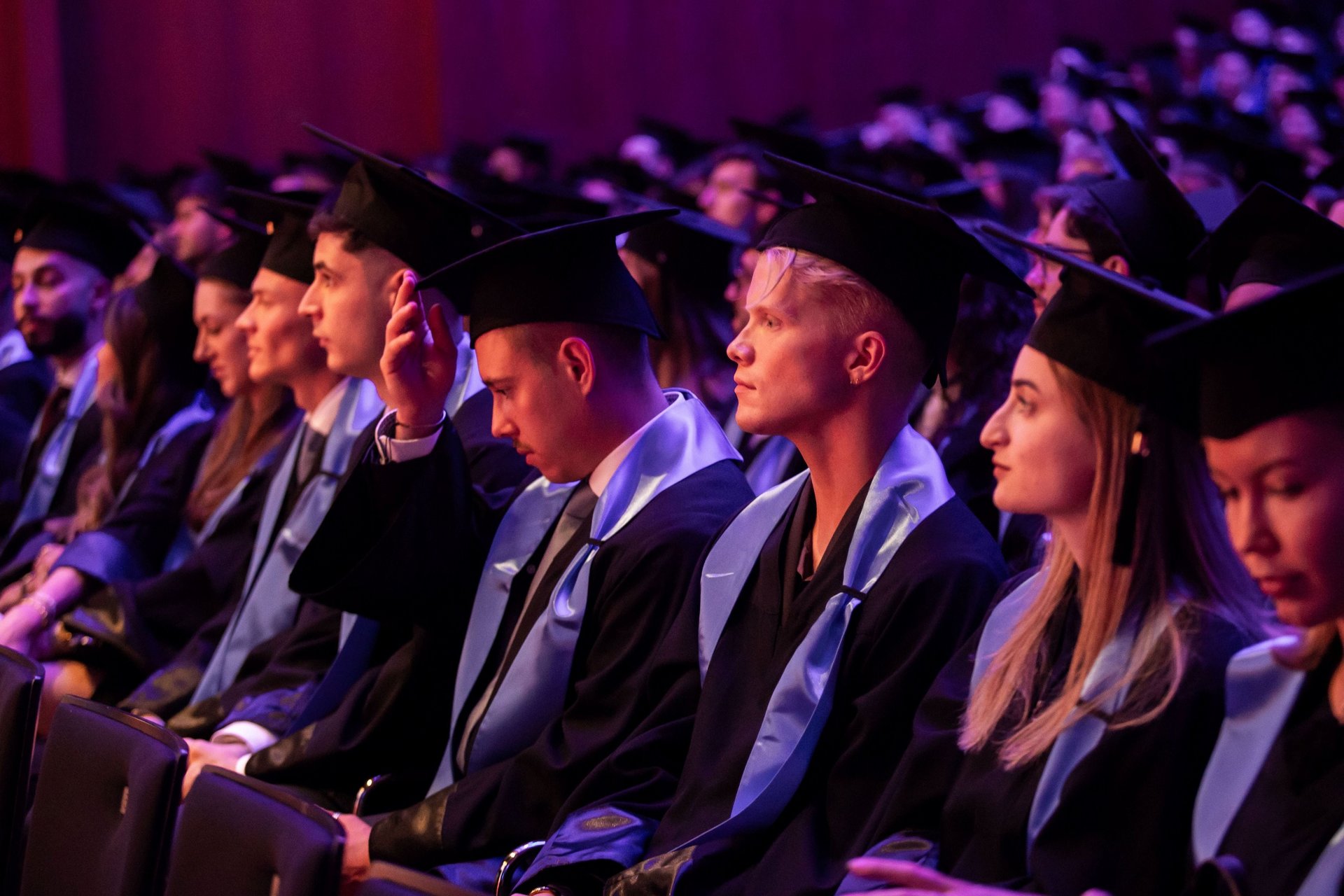 Absolventinnen und Absolventen sitzen in Reihen und hören die Laudatio
