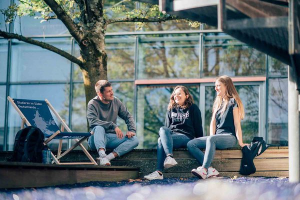 Studierende sitzen auf dem Campus in der Sonne